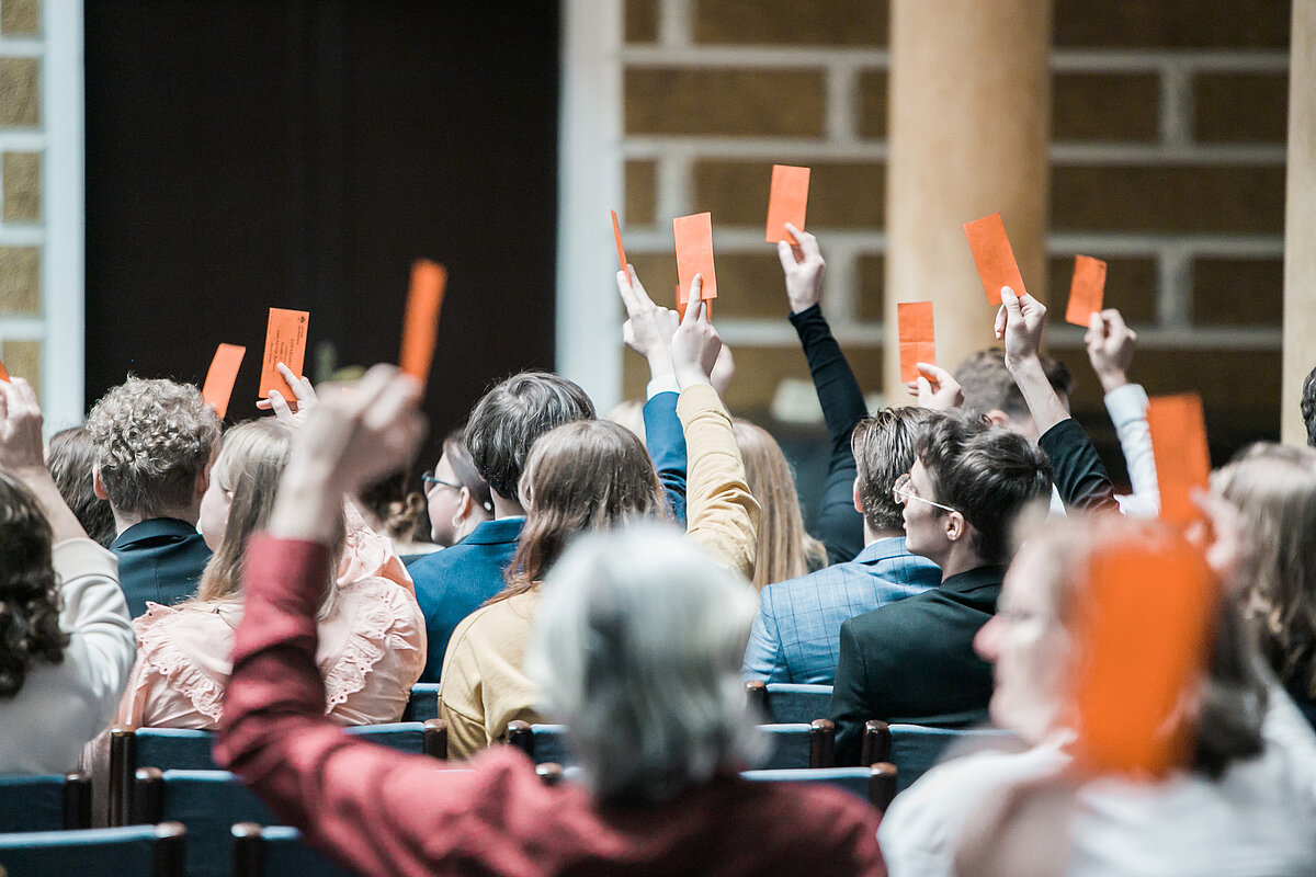 Balsošanas process Satversmes sapulcē.
Foto: Toms Grīnbergs. LU Cilvēki piedalās atklātā balsojumā, paceļot gaisā sarkanas balsošanas lapiņas.