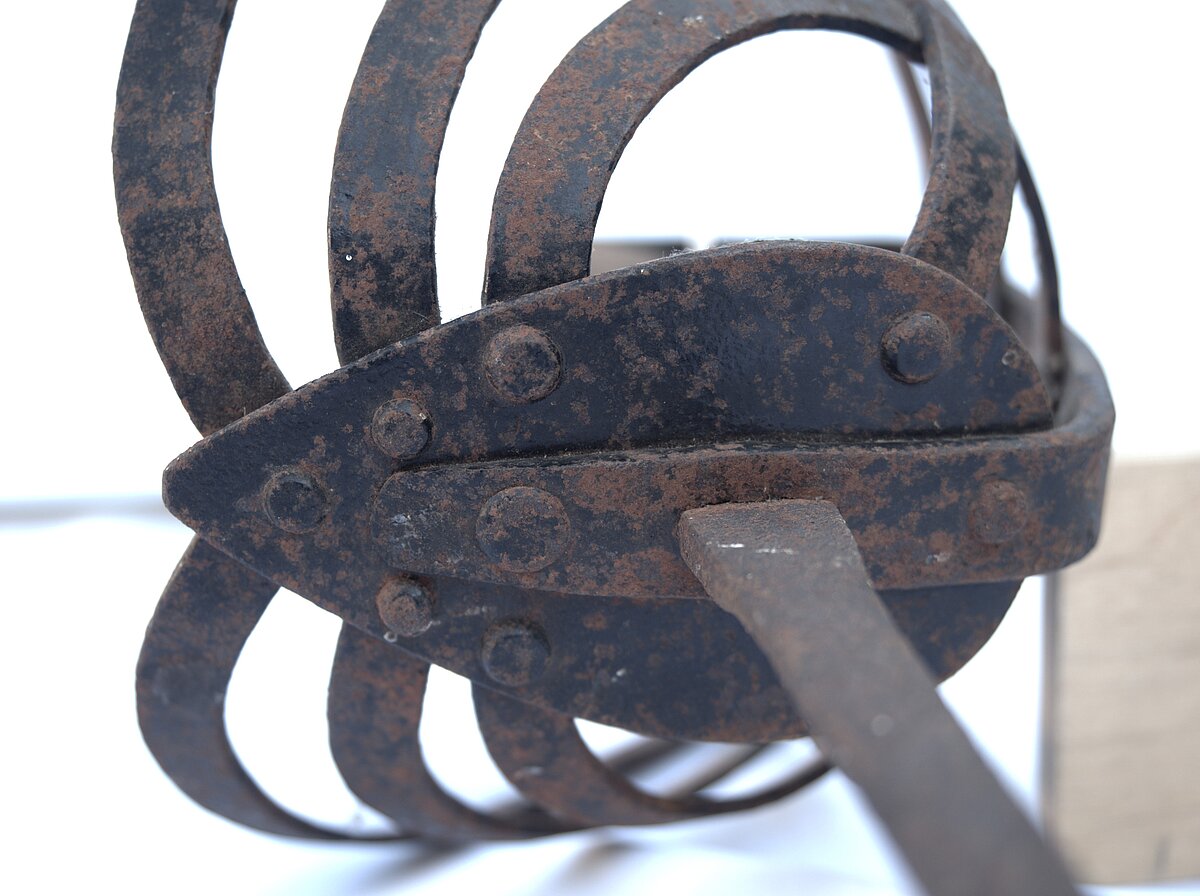 6. att. Rapiera šķērša daļa ar korozijas bojājumiem un daļēji saglabājušos krāsojuma slāni. Foto: Gints Ajausks 6. att. Rapiera šķērša daļa ar korozijas bojājumiem un daļēji saglabājušos krāsojuma slāni. Foto: Gints Ajausks