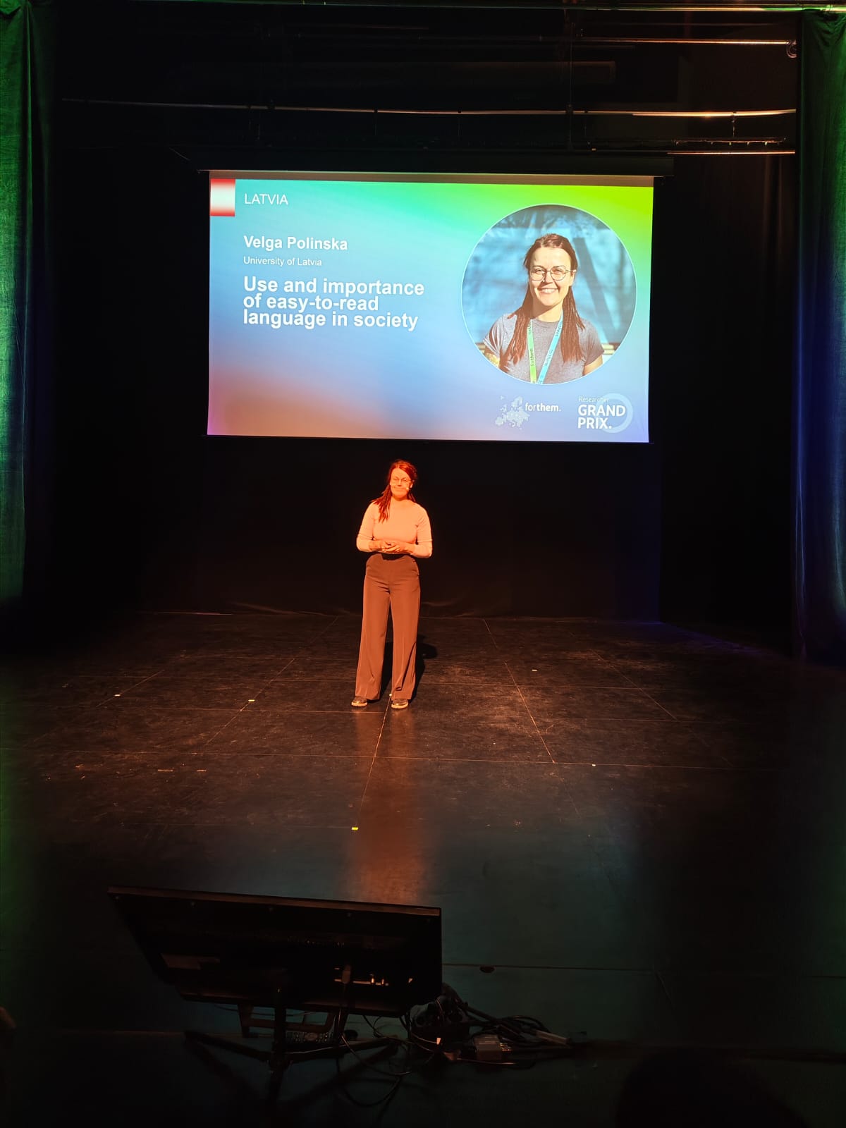 Velga Polinska uz skatuves, fonā prezentācija